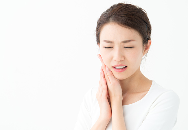 歯が痛み頬に手を当てる女性